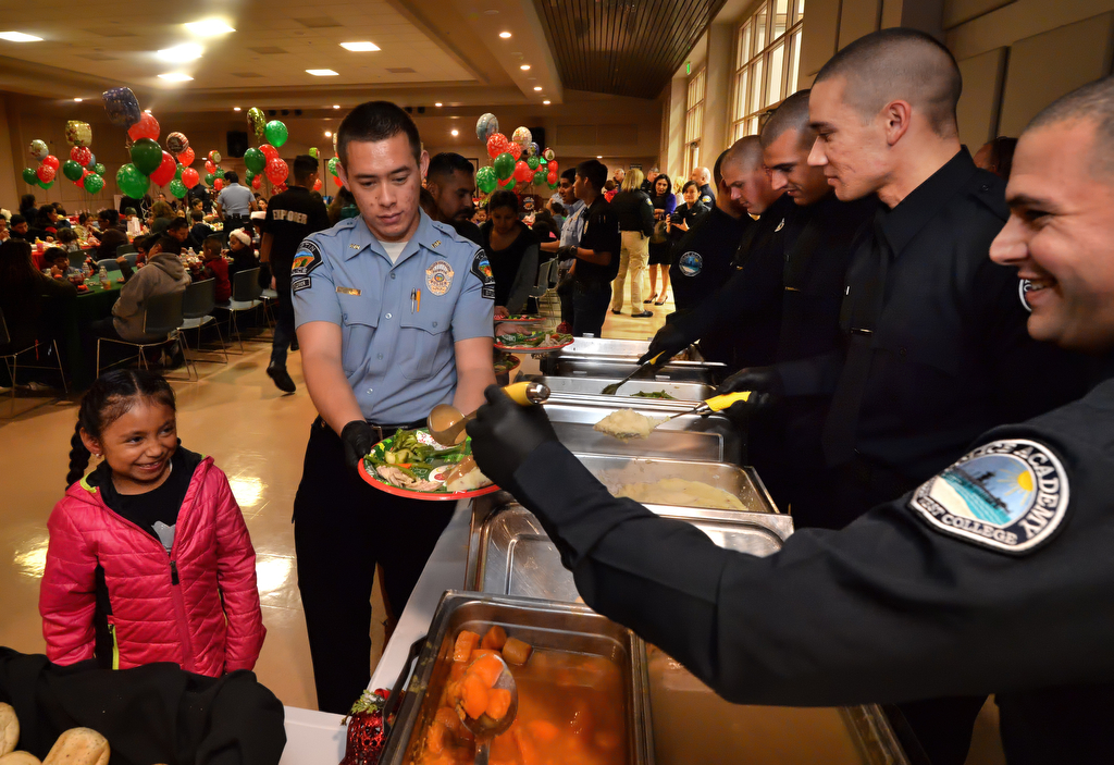 Six-year-old Esmeralda Sanchez of Tustin gets a little help with her holiday meal from Tustin PD Explorer Andrew Hollister during Tustin PD’s annual “Santa Cop” at the Tustin Community Center. Photo by Steven Georges/Behind the Badge OC