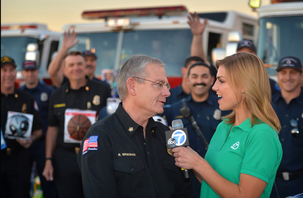 Anaheim Fire & Rescue Chief Randy Bruegman talks to Bri Winkler of ABC7 Eyewitness News during a live TV spot for the Spark of Love Toy Drive at the Honda Center in Anaheim. Photo by Steven Georges/Behind the Badge OC