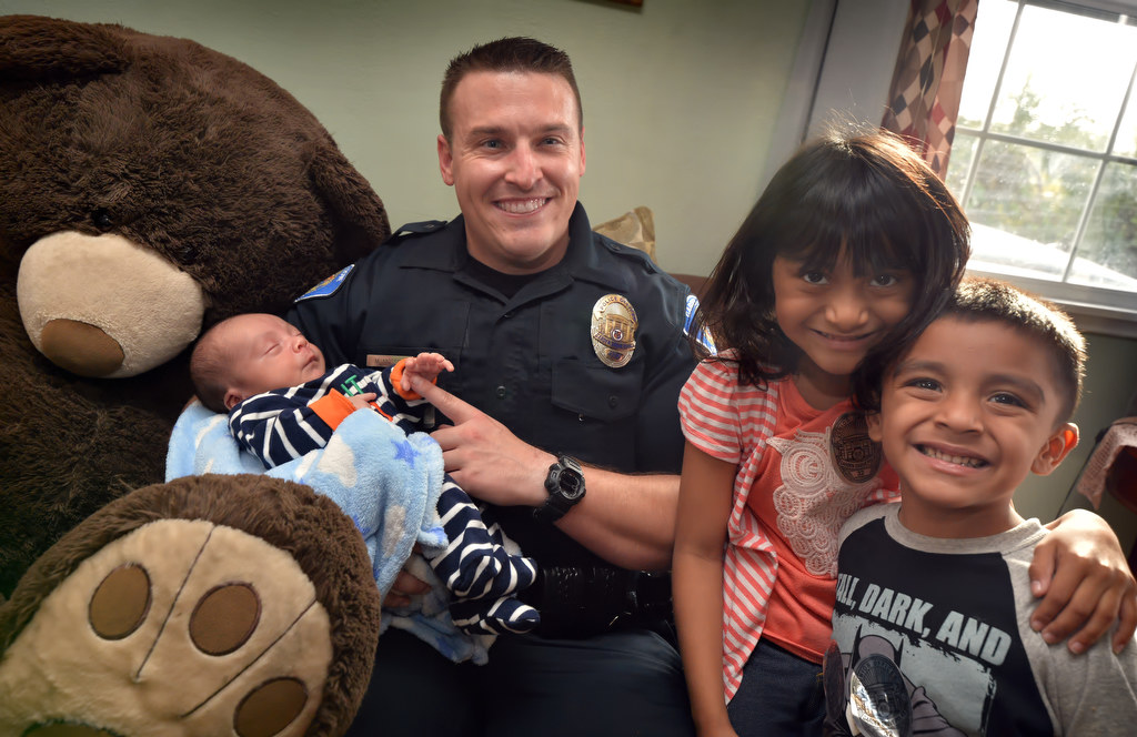 Garden Grove PD Officer Mitchel Mosser with 3-week-old Gabriel Barragan, Emily Barragan, 5, and Matthew Barragan, 3. Garden Grove officers brought the Barragan family Christmas presents (including the big Teddy bear, left) after their mother, Erika, passed away the day after giving birth to Gabriel. Photo by Steven Georges/Behind the Badge OC