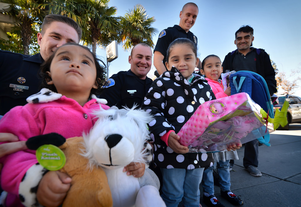 Genisis, 1, left, her sisters Belinda, 3, Janet 5, and their father Alfredo Monsivaiz, far right, hold their new Christmas presents given to them by Garden Grove officers Danny Mihalik, back left, Nick Lazenby and Gerald Jordan, at the Garden Grove Inn on Christmas day. Photo by Steven Georges/Behind the Badge OC