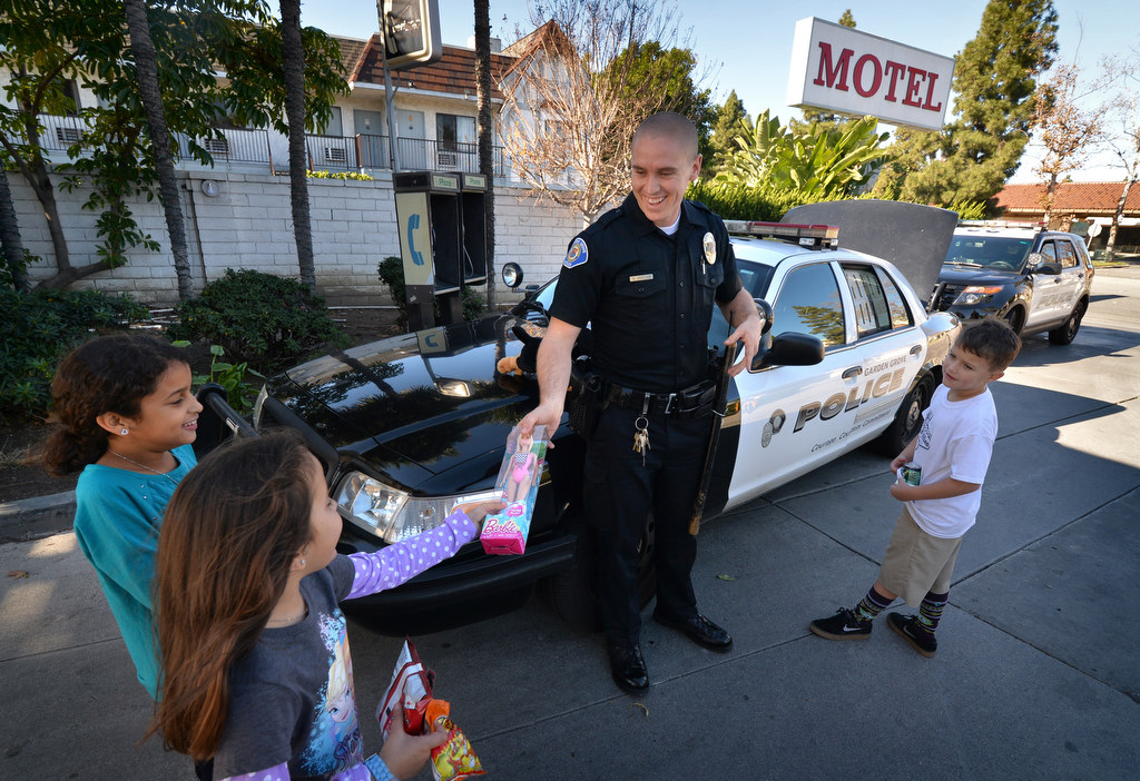 Garden Grove PD Officer Gerald Jordan hands out Christmas presents at the Garden Grove Inn on Christmas day to Iris Hall, 9, left, her sister Katie Hall, 7, and Jaedy Bird, 7, far right. Photo by Steven Georges/Behind the Badge OC
