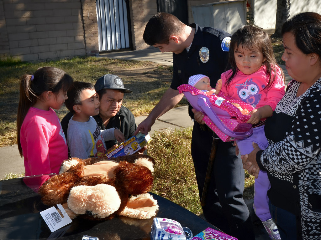 Garden Grove Officer Ben Elizondo helps hand out presents during Christmas day on Buena St. to Bianca Hernandez, 6, left, her brother Gustavo Hernandez, 4, Augustin Hernandez, their dad, and Alexa Hernandez, 2. Photo by Steven Georges/Behind the Badge OC