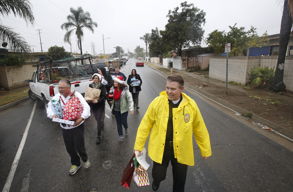 Retired Anaheim Police Captain Joe Vargas, left, and Captain Jarrett Young, right, brave the rain with Spencer and Rebecca Holbrook, Jennifer Vargas, Chad Hammitt  and Maria Rodriguez to deliver Christmas gifts to needy children in Anaheim. Photo by Christine Cotter/Behind the Badge OC