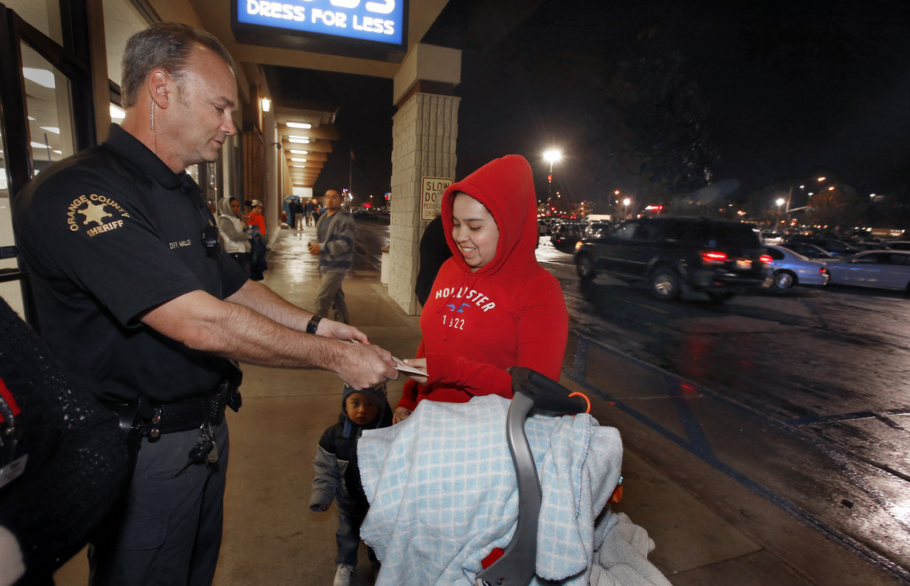 Orange County Sheriff's Deputy Ryan Miller hands a cash gift to Tina Garcia at a shopping center in Lake Forest. Thanks to an anonymous donor, the Orange County Sheriff's Department gave hundred dollar bills to needy families during the Christmas holiday. Photo by Christine Cotter/Behind the Badge OC