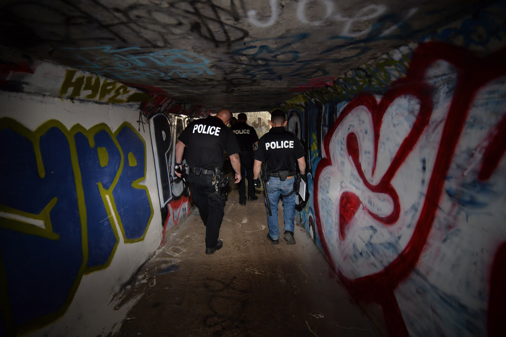 Officers from Fullerton PD, left, and La Habra PD walk through narrow flood control tunnels covered in graffiti near Harbor Blvd. and Imperial Hwy. looking for homeless people that might be living there, which would be dangerous should it rain. Photo by Steven Georges/Behind the Badge OC