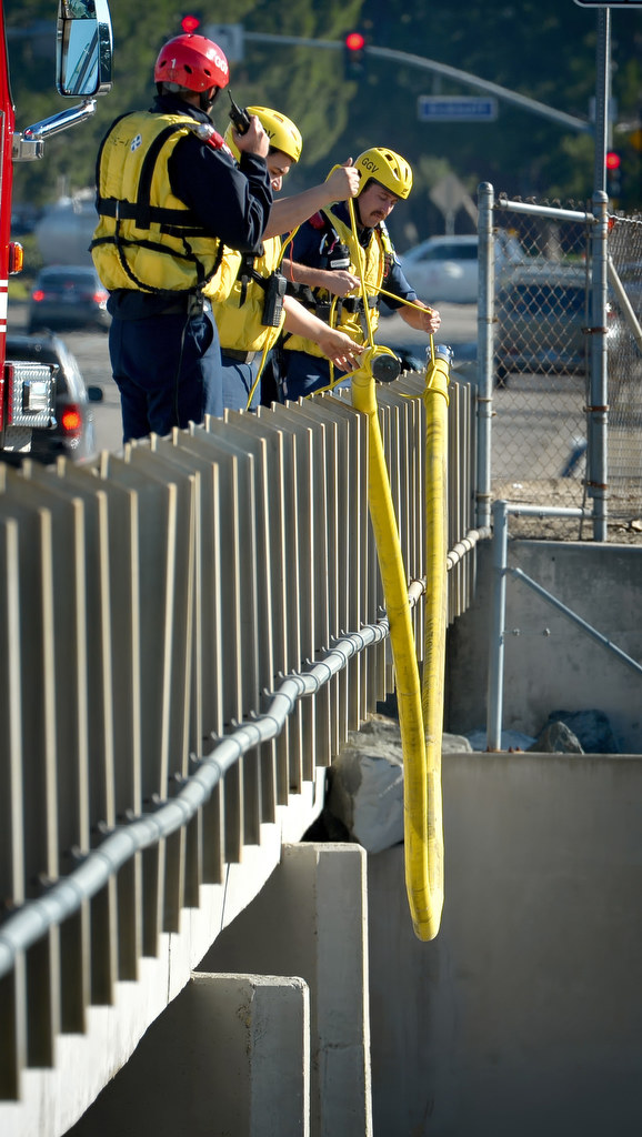 Garden Grove Fire Rescue Workers lower a firehose over the side of the Orangewood Ave. bridge of the Santa Ana River to be used as a floating rescue line during a swift water rescue drill. Photo by Steven Georges/Behind the Badge OC