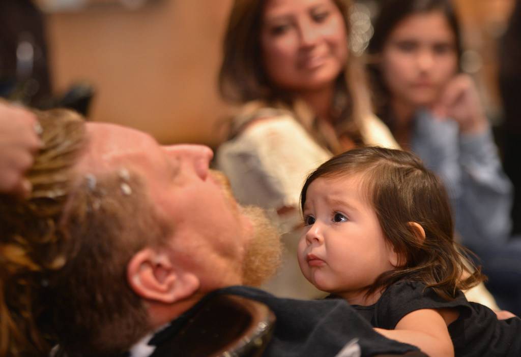One-year-old Makayla Salazar climes up to take a close look at her daddy, Garden Grove Police Corporal Sean Salazar, as he gets his first haircut in over five years now that he is coming off his undercover narcotics assignment and is returning to patrol. Watching behind them is his wife Rachel Salazar and his other daughter Madison Tucker. Photo by Steven Georges/Behind the Badge OC