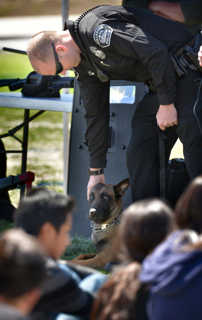 Fullerton Police Officer Scott Flynn leans over to pet his k-9 police partner Jax, a Belgian Malinois, before giving a demonstration for the kids attending the OC GRIP soccer camp at Cal State Fullerton. Photo by Steven Georges/Behind the Badge OC