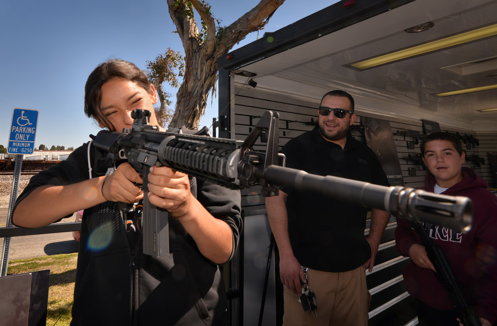 Isabel Avalos, 14, of Fullerton, tries out an Air Soft Gun (without projectiles) under the supervision of KWAÕs Jesse Gonzalez, behind her, during the Shoot Or DonÕt Shoot Law Enforcement Challenge. Photo by Steven Georges/Behind the Badge OC