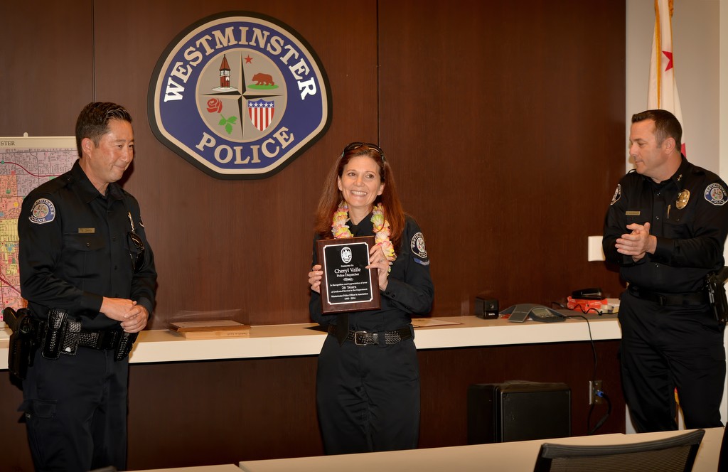 Westminster PD Officer Mike Ogawa, left, and Acting Chief Dan Schoonmaker honor Dispatcher Cheryl Valle for her 26 years of service during her retirement ceremony. Photo by Steven Georges/Behind the Badge OC