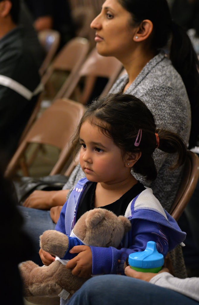 Three-year-old Maya Williams holds a teddy bear as she attends an Anaheim Police community meeting at Crescent Elementary School with her mother, right just outside the photo, and her friend Roshni Patel, behind her, as police discuss last week’s fatal shootings at a nearby park.  Maya’s older brothers attend the school. Photo by Steven Georges/Behind the Badge OC