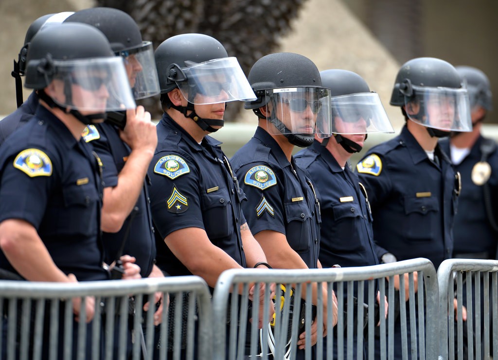 Anaheim Police Officers put on protective helmets after a full water bottle was thrown at the police. The protest crowd did keep to their side off the barricade in front of the Anaheim Convention Center. Photo by Steven Georges/Behind the Badge OC