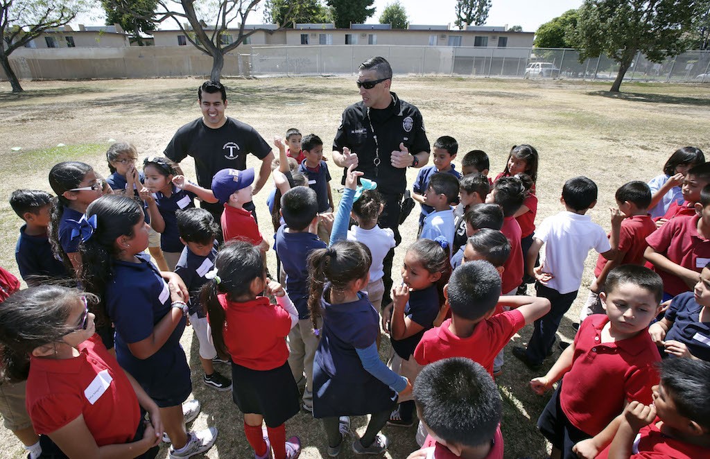 Heideman Elementary school students gather around Tustin Police officers Michael Carter and Matthew Roque during a community outreach run club at the school.  Photo by Christine Cotter/Behind the Badge OC 