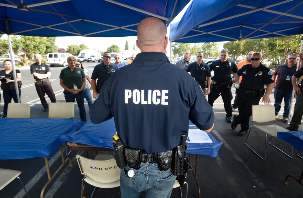 Garden Grove PD Officer Brian Hatfield briefs the task force on how to handle the homeless with respect before walking down to the flood canals behind Calvary Chapel on Knott Ave. where the homeless are living. The tents and tables setup ahead of time are so the health care professionals can talk to the homeless about services available to them. Photo by Steven Georges/Behind the Badge OC