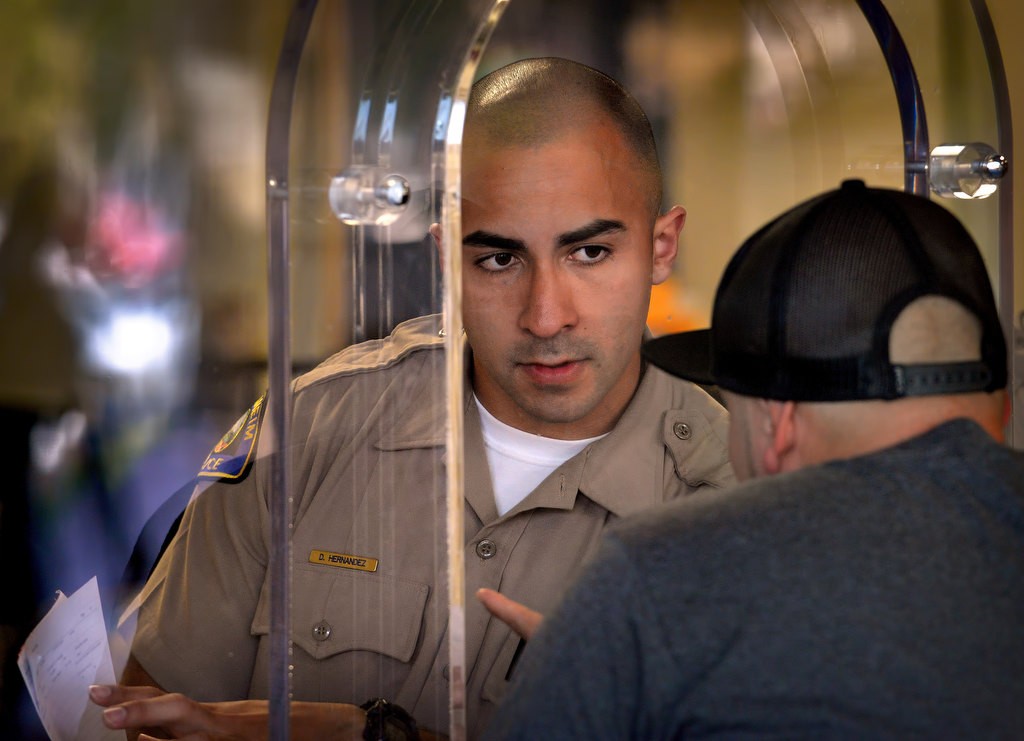 Anaheim PD Cadet David Hernandez helps a man at the front counter of the Harbor police headquarters. Cadets helping the public at the front desk helps free up sworn officers to perform other duties. Photo by Steven Georges/Behind the Badge OC