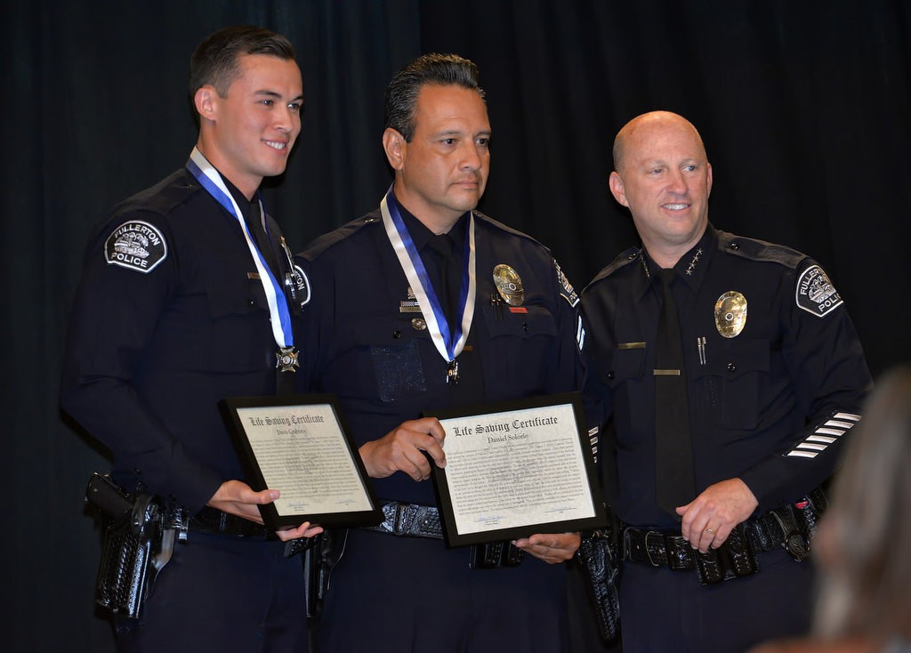 Officer David Crabtree, left, and Cpl. Daniel Solaria both receive the Life Saving Medal from Chief Dan Hughes for saving an 8-week-old infant from a distraught man threatening to throw the baby over a second story stairway railing yelling, “I want to kill him.” Both officers wrapped their arms around the suspect to keep him from throwing the infant over the railing to certain death. Photo by Steven Georges/Behind the Badge OC