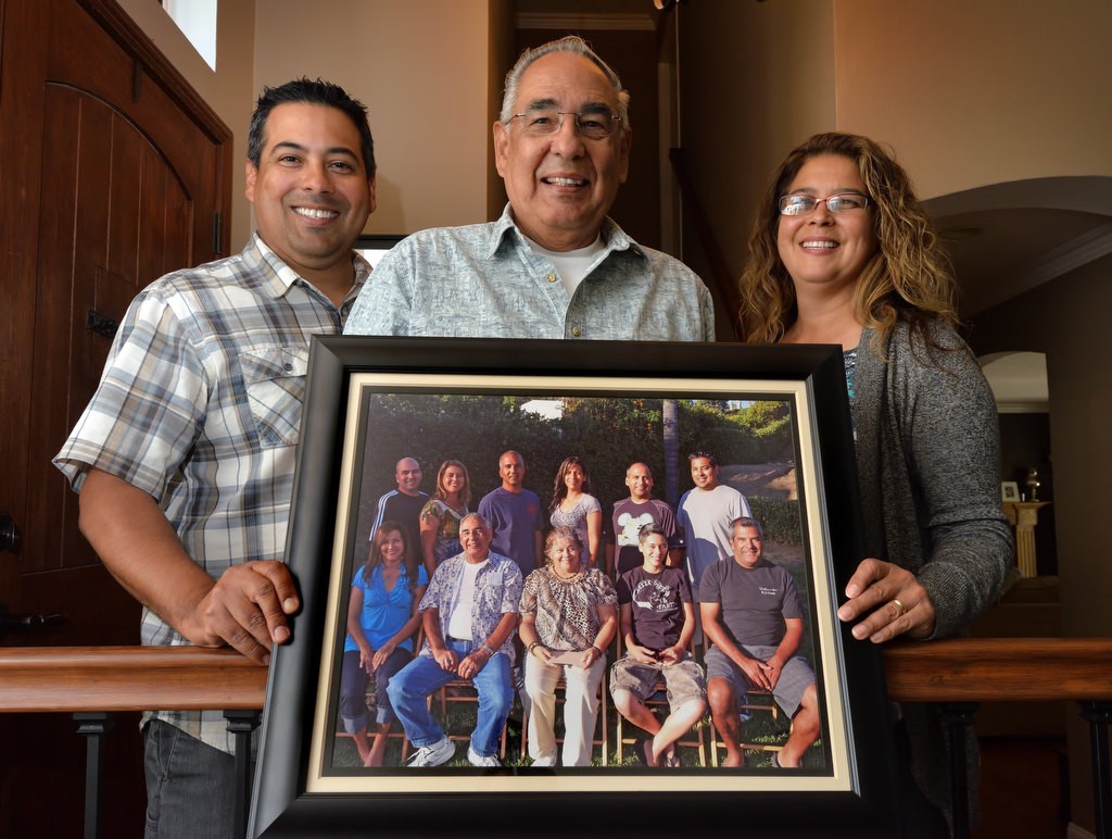 Ron Reyes, retired from the Orange County Sheriff Department, center with two of his kids, Paul Reyes, Carlsbad PD, and Roberta Granek, Litenant Los Angeles Sheriff Department holding a family photo taken in 2011 showing all nine of his kids who all went into law enforcement. One did later switch to firefighting. In the photo they are holding is front row from left, Yvonne Shannon, LASD, Mike Reyes, LASD, Veronica Reyes, mom, Yvette Reyes, LASD, and Paul Reyes, Carlsbad PD. Back row from left, Joe Reyes, LASD, Roberta Granek, Lieutenant LASD, Mike Reyes, LAFD, Rebecca Reyes, LASD, Edward Reyes, LASD, and Ron Reyes, OCSD. Photo by Steven Georges/Behind the Badge OC