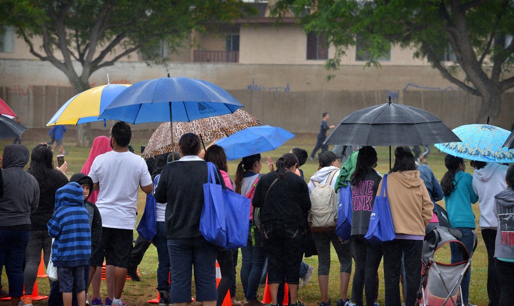 Family members watch with umbrellas as kids from Robert Heideman Elementary round the track during Tustin PD’s Run Club. Photo by Steven Georges/Behind the Badge OC