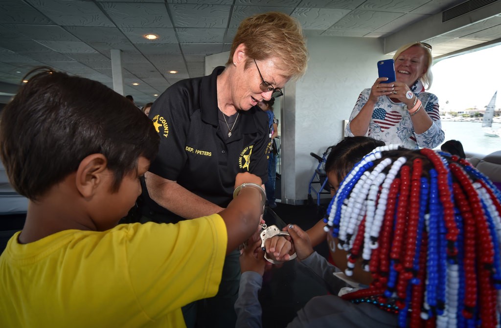 Orange County Sheriff Dep. Peters slaps handcuffs on Make-a-Wish kids, at their request, as they play during a 4th of July Newport Harbor Cruise. Photo by Steven Georges/Behind the Badge OC