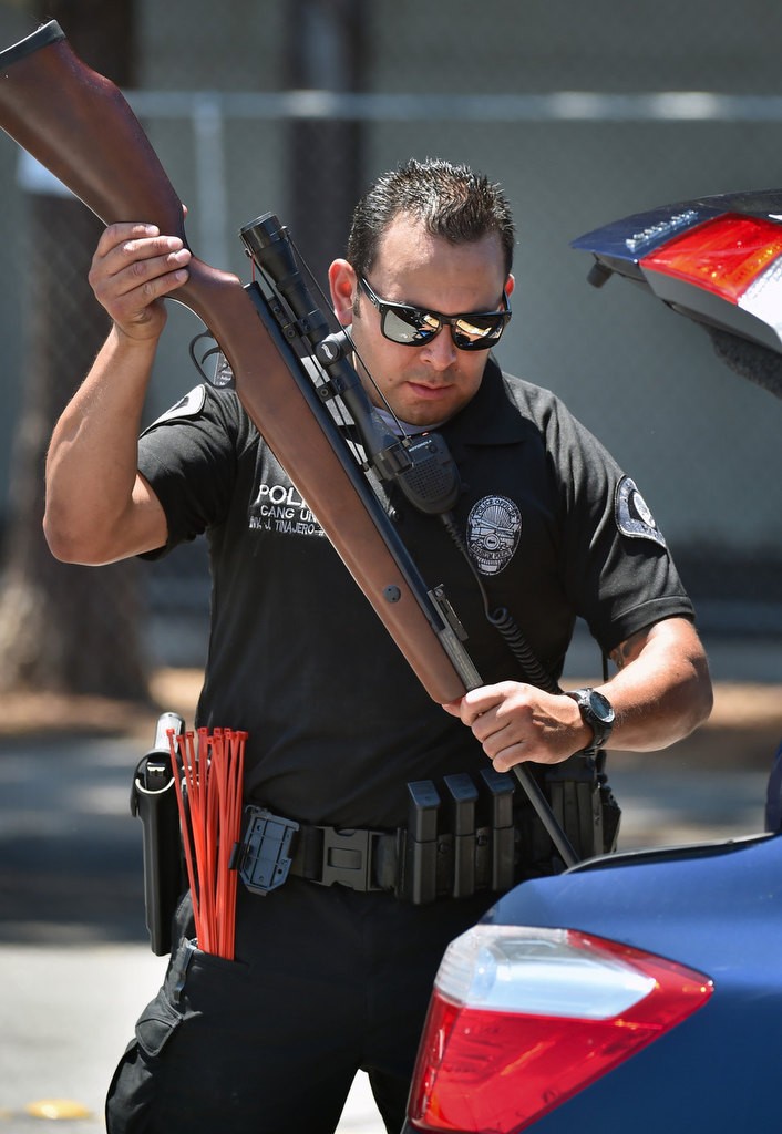 Officer Joie Tinajero inspects a rifle with a scope for safety before inserting a red tie to prevent the weapon from firing. After the guns are confirmed safe, the car drives to the next station where the guns are collected. Photo by Steven Georges/Behind the Badge OC