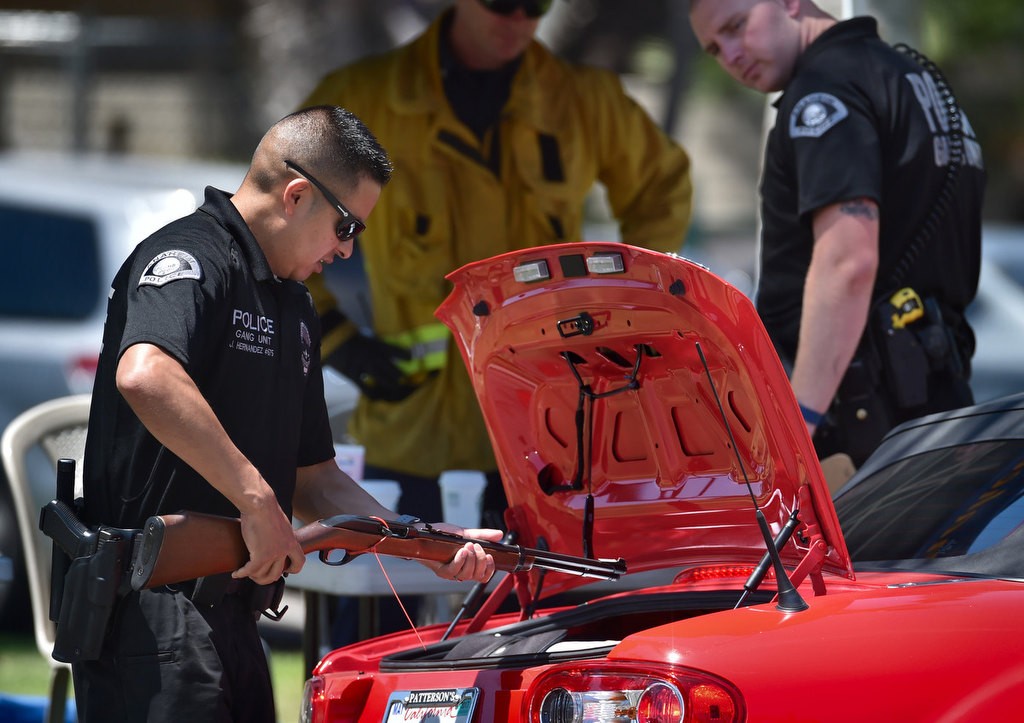 Officer J. Hernandez removes a rifle from the trunk of a car during Anaheim PD’s gun buyback program at La Palma park. Photo by Steven Georges/Behind the Badge OC