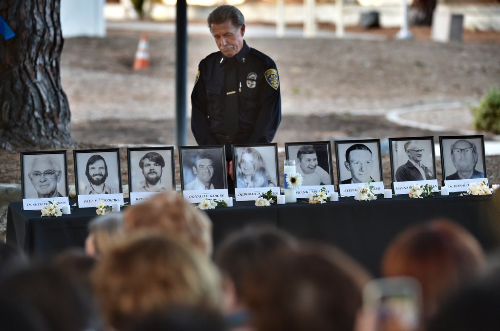 CSUF’s Chaplain Paul Miller stands behind photos of the seven killed and two wounded in the 1976 CSUF campus shootings, displayed at the 40th anniversary remembrance ceremony at Memorial Grove. Photo by Steven Georges/Behind the Badge OC