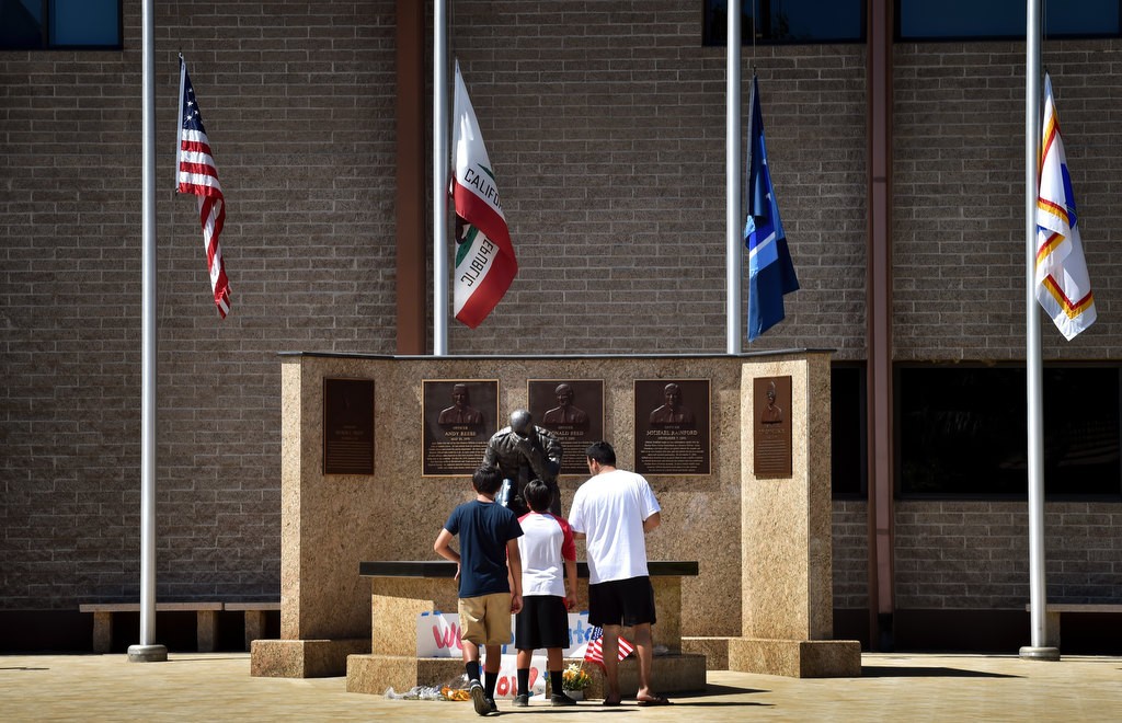 Emilio Arenas of Garden Grove looks over the banner and flowers left at the Garden Grove Police memorial at police headquarters with his sons Jonathan Arenas, 12, left, and Andrew Arenas, 10. Photo by Steven Georges/Behind the Badge OC