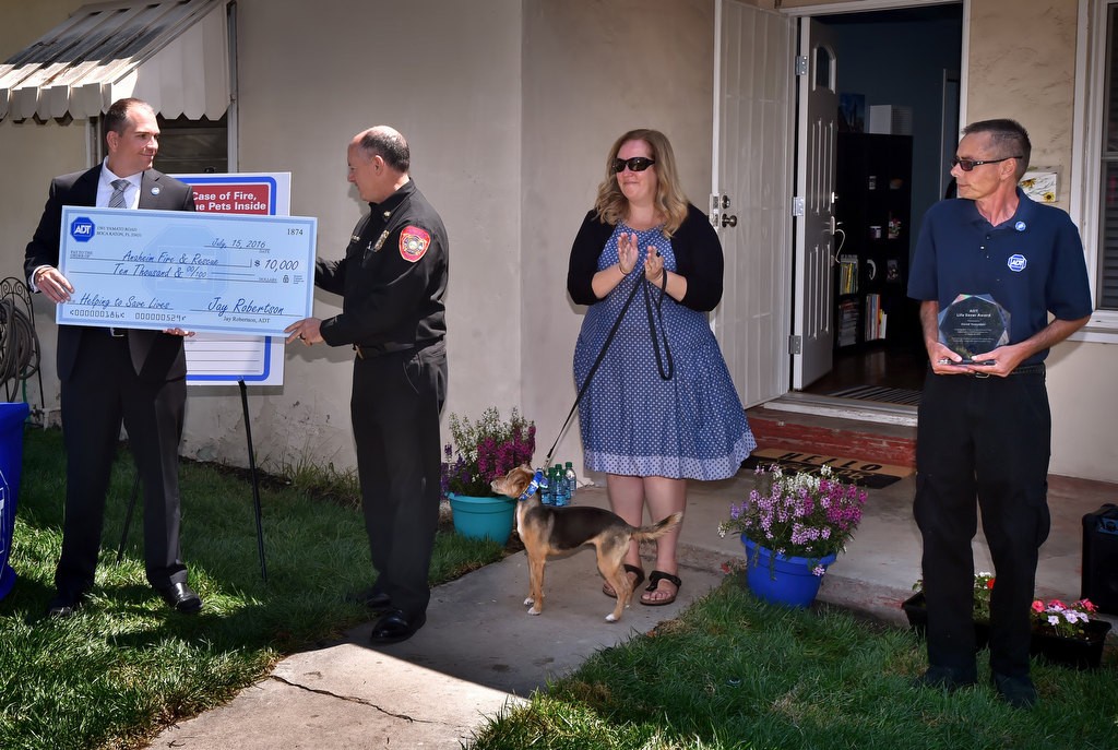 Bob Tucker, director of Corporate Affairs for ADT, left, presents a check for $10,000 to Anaheim Fire & Rescue’s Deputy Chief Rusty Coffelt for the department’s rescue of Fiona, an 8-year-old dog, form a house fire under surveillance by ADT. Next to them is the homeowner Amber Cooper, with her dog Fiona, and David Tompkins, the ADT dispatcher who made the call to AF&R. Photo by Steven Georges/Behind the Badge OC