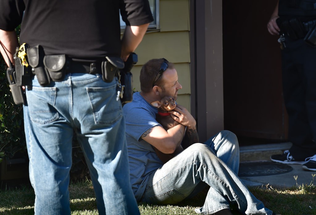A man on parole sits outside while holding his dog as police conduct a routine search inside inside his apartment. No violations were found. Photo by Steven Georges/Behind the Badge OC