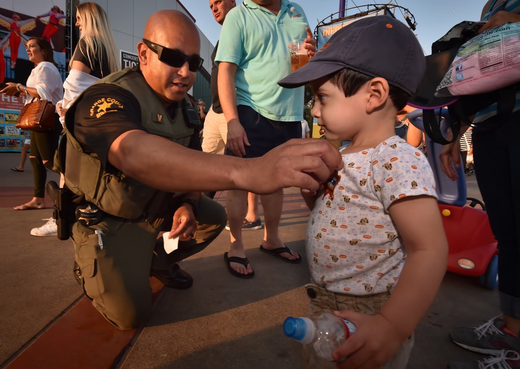 OC Sheriff Dept. Dan Villa kneels down to give 5-year-old Daniel Serrano of Santa Ana a sheriff sticker at the OC Fair. Photo by Steven Georges/Behind the Badge OC