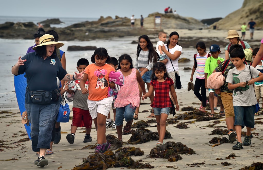 Laguna Beach’s Marine Safety Tide Pool Educator Amee Penso, left, leads the Orange County Family Justice Center Foundation kids through the seaweed and tide pools at Laguna Beach. Photo by Steven Georges/Behind the Badge OC