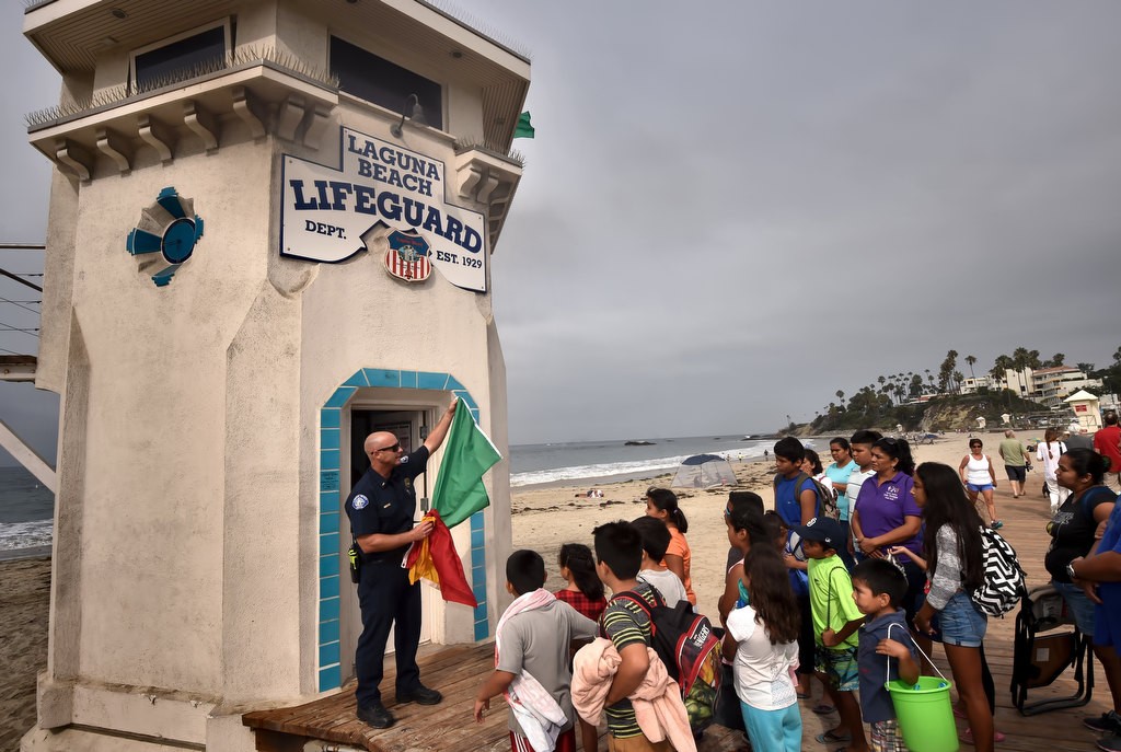 Laguna Beach Lifeguard Lt. Kai Bond stands in front of the lifeguard tower built in 1929 as he shows the Orange County Family Justice Center Foundation kids the various color flags and what they mean during a field trip to the beach and tide pools at Laguna Beach. Photo by Steven Georges/Behind the Badge OC