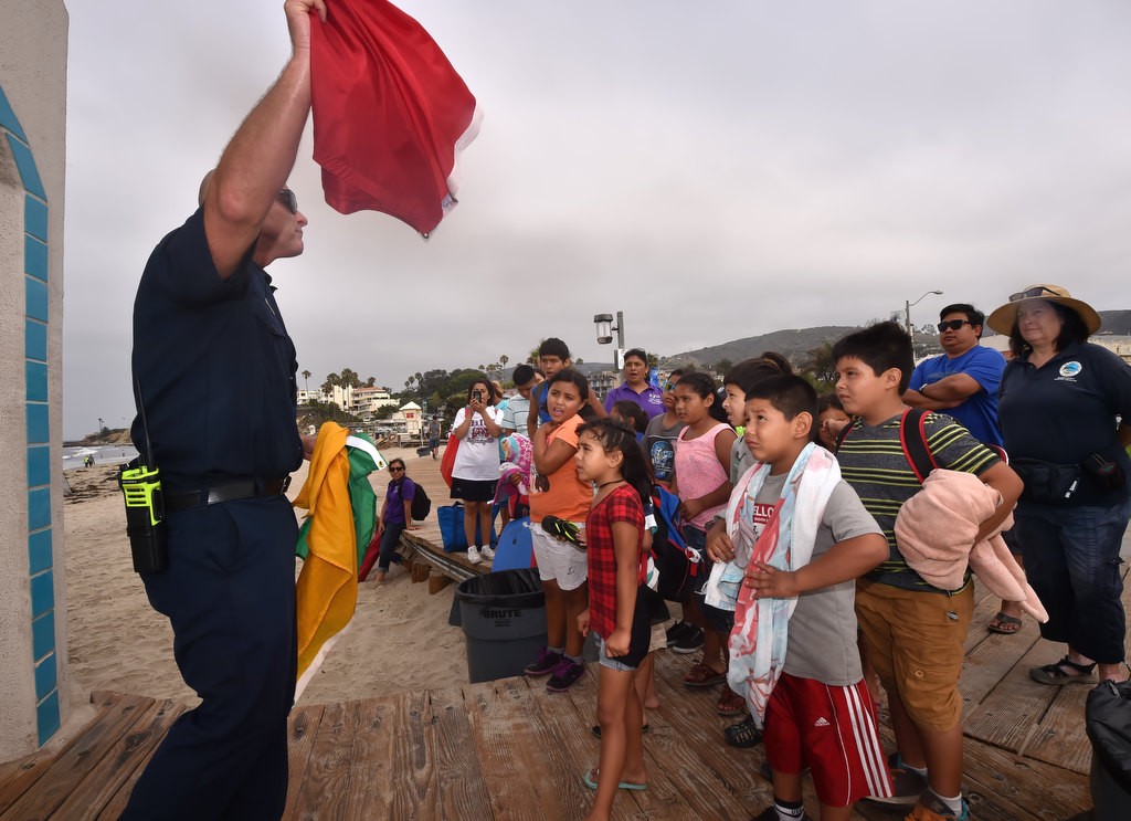 Laguna Beach Lifeguard Lt. Kai Bond stands in front of the lifeguard tower as he shows the Orange County Family Justice Center Foundation kids the various color flags and what they mean during a field trip to the beach and tide pools at Laguna Beach. Photo by Steven Georges/Behind the Badge OC
