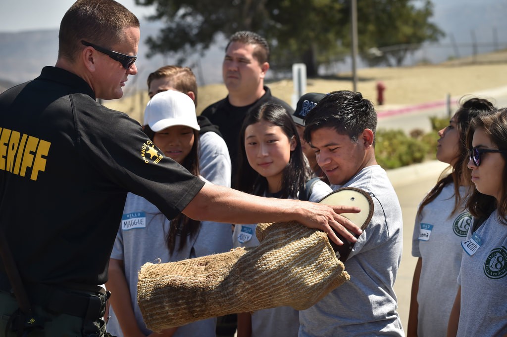 Roberto Santos, 17, tries on a K-9 decoy arm, used for police dogs in training to bite, with the help of OC Sheriff Deputy Ryan Buhr during a Youth Citizens’ Academy tour of the Loma Ridge Emergency Operations Center. Photo by Steven Georges/Behind the Badge OC