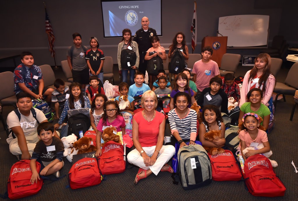Susan Bruegman, Family Justice Center Foundation board member, front center, and Anaheim PD Lt. James Kazakos, back center, with OCFJC Foundation kids after they received their new back to school backpacks. Photo by Steven Georges/Behind the Badge OC