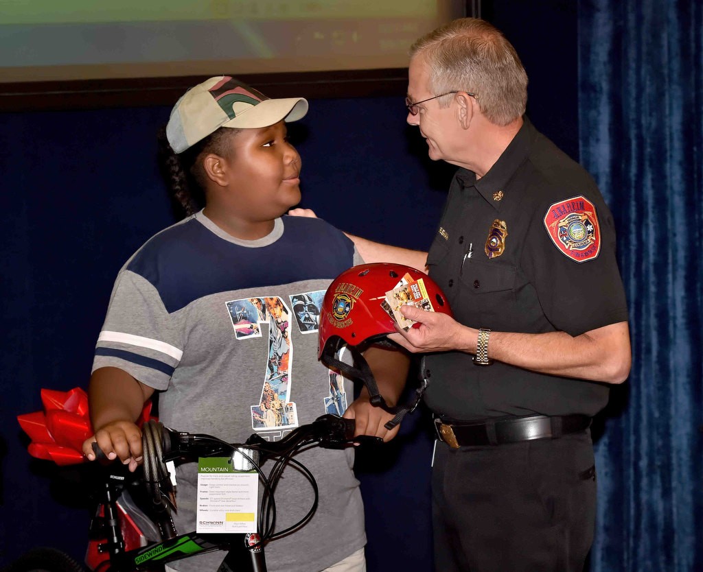 Anaheim Fire & Rescue Chief Randy Bruegman provides 10-year-old Daniel Cowboy with a special Anaheim Fire & Rescue bicycle helmet for his new bicycle, part of the department’s helmet safety campaign, during a press conference to announce Anaheim PD reinstating the bicycle registration program. Photo by Steven Georges/Behind the Badge OC