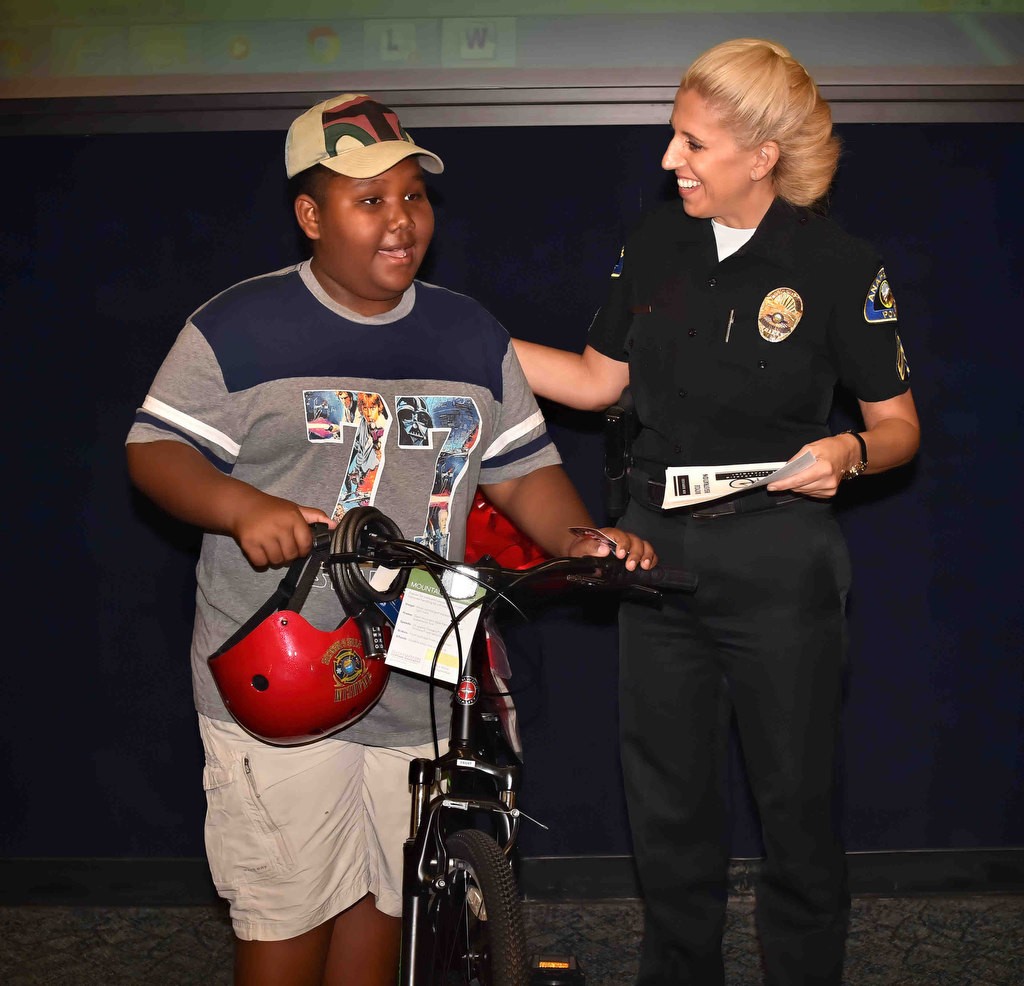 Ten-year-old Daniel Cowboy smiles as he is presented with a new bicycle from the Anaheim PD, and Officer Sarah Shirvany, right, after his old one was stolen, during a press conference to announce Anaheim PD reinstating the bicycle registration program. Photo by Steven Georges/Behind the Badge OC
