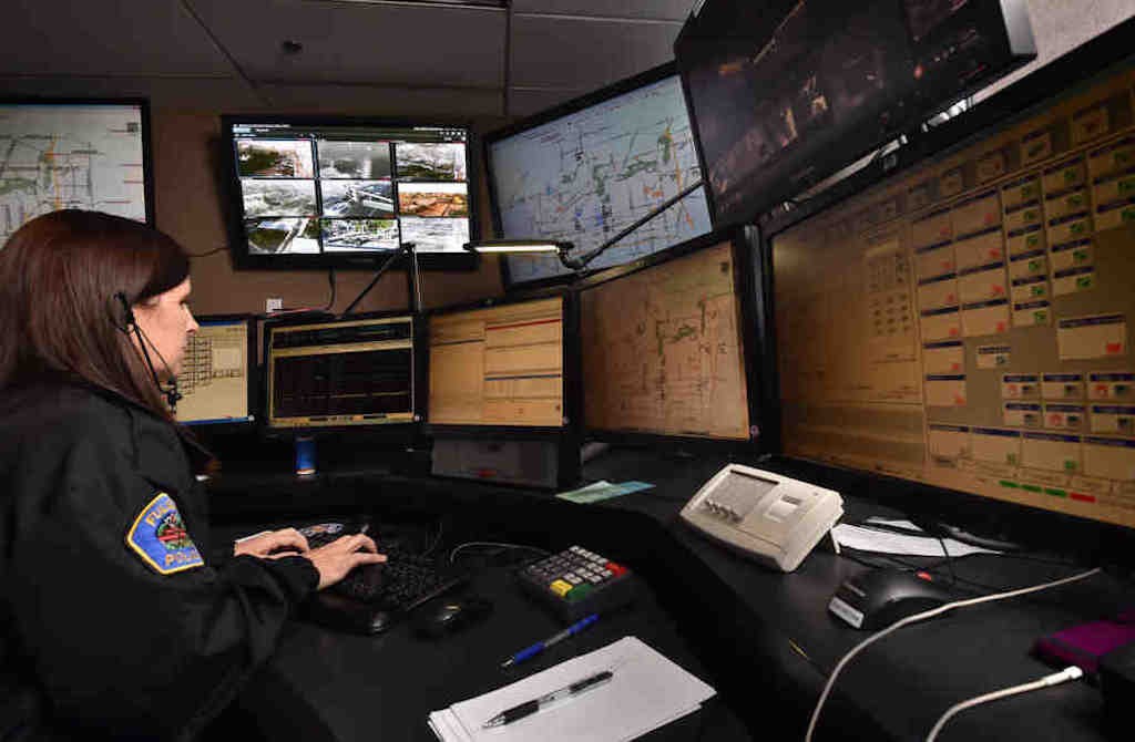 Fullerton PD Dispatcher Rodriquez works the radio dispatch station with computer screens that show calls being worked on, a map showing where patrol cars are located and even a screen displaying the scene from cameras that are placed around police headquarters and throughout the city. Her station talks to and assigns officers to calls while other dispatchers take the calls from the public. Photo by Steven Georges/Behind the Badge OC