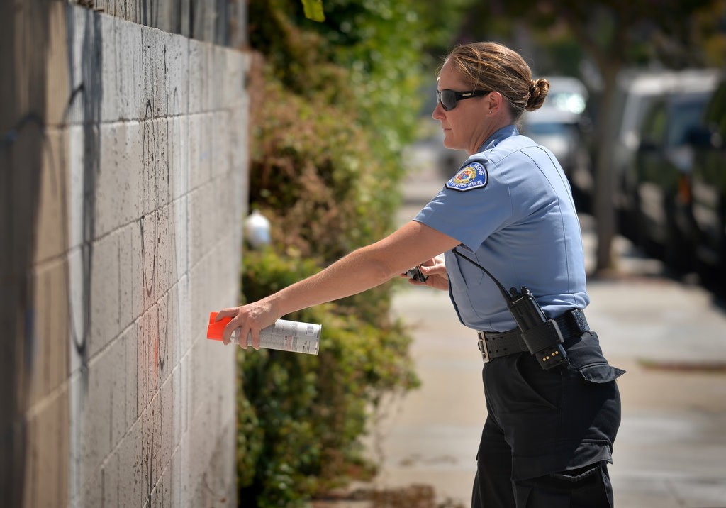 Garden Grove PD CSO Kari Flood uses a spray paint can to mark a grafted wall with an orange dot to tell other officers that a report has already been taken. Graffiti on public property are placed in a list to be cleaned up and/or painted over. Photo by Steven Georges/Behind the Badge OC