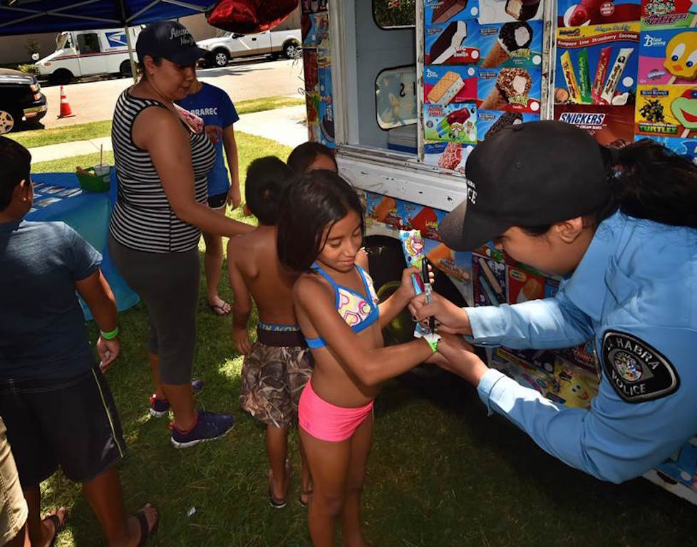 La Habra Police Aid Larissa Terrones, right, marks wrist bands as kids attending La Habra PD’s Cool Cops community outreach gathering get a free ice cream. Photo by Steven Georges/Behind the Badge OC