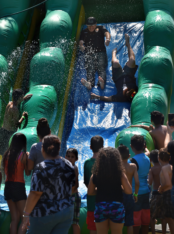 La Habra PD Det. Daniels, left, and Jake Lujan of of La Habra Parks and Recreation go down the water slide together to the cheers of the kids. Photo by Steven Georges/Behind the Badge OC