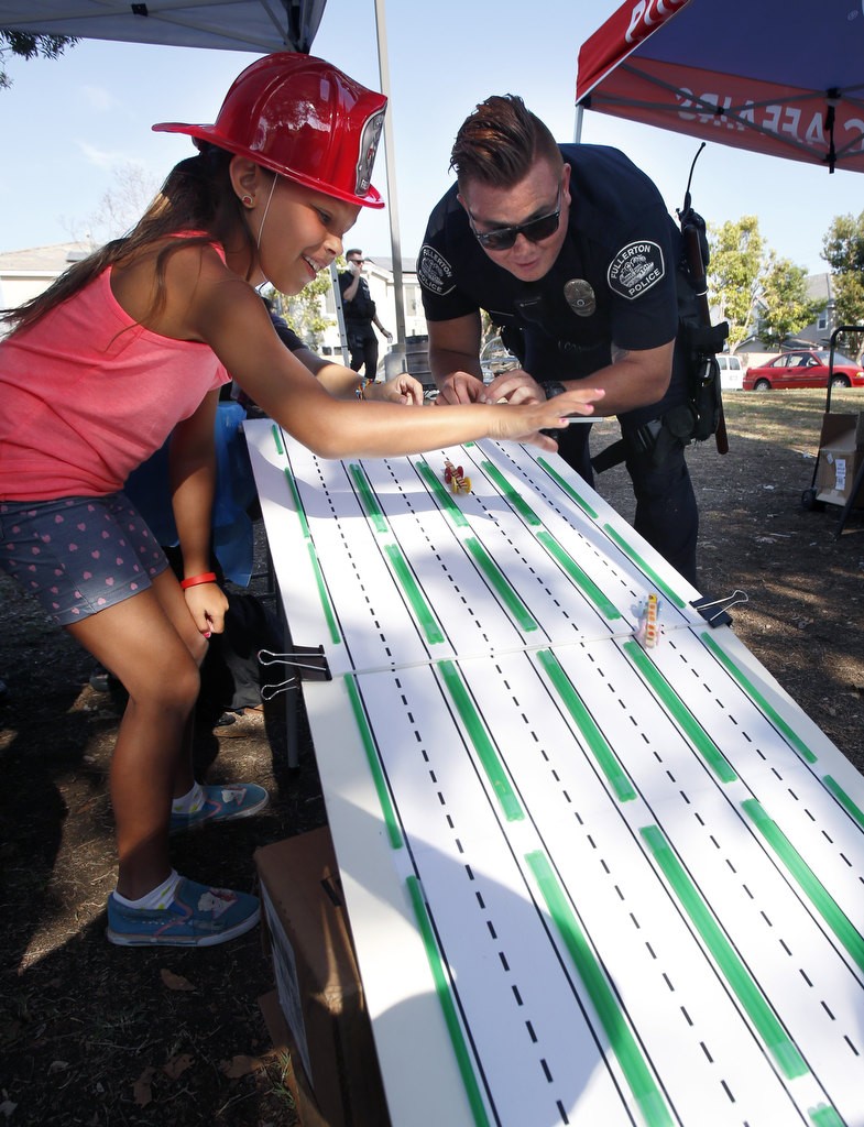 Fullerton PD Officer Jose Paez races miniature cars with nine year-old Sophia Blake during National Night Out at Independence Park. Photo by Christine Cotter