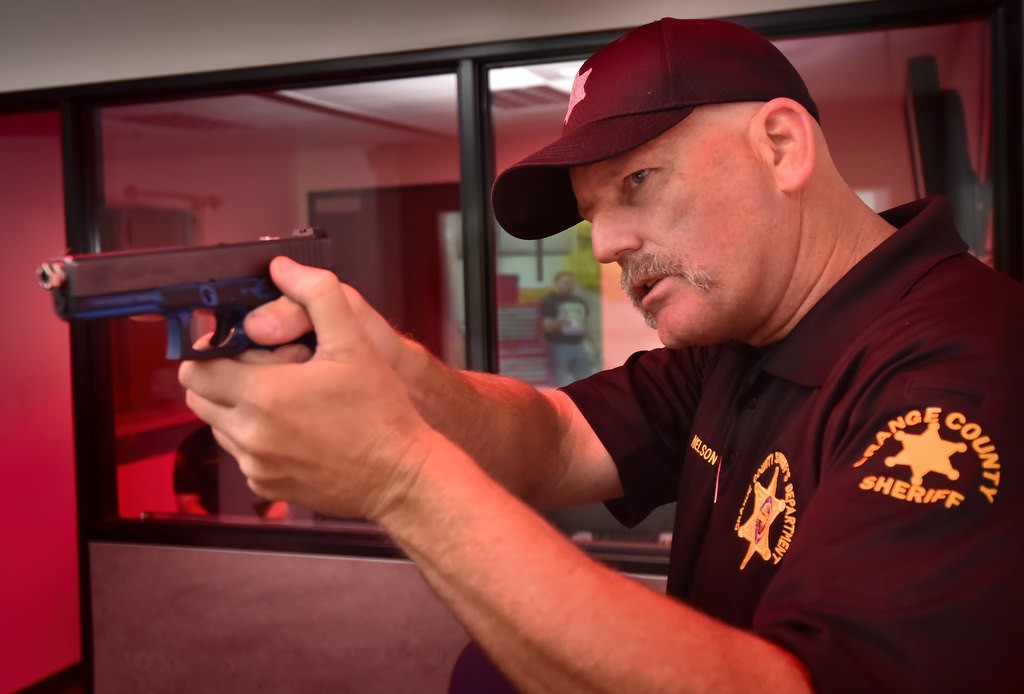 Sgt. Richard Nelson of the OC Sheriff’s Department instructs a group of kids from the Youth Citizens’ Academy on the proper way to hold a hand gun before giving them their turn with shooting simulator at the Orange County Sheriff's Training Center. Photo by Steven Georges/Behind the Badge OC