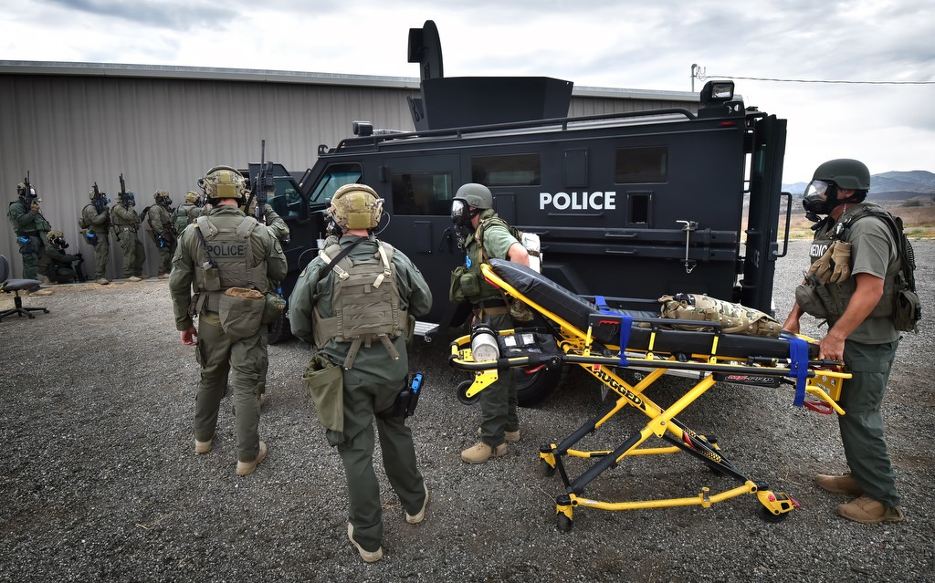 North County SWAT members, Fullerton Firefighter/Medic Mike Lemmon and Brea Engineer/Medic Bill Schaefer, right, wait behind the BearCat (SWAT vehicle) for protection as they stand by to receive a simulated wounded officer as other SWAT members, left, get ready to enter a building during a North County SWAT drill in Irvine. Photo by Steven Georges/Behind the Badge OC