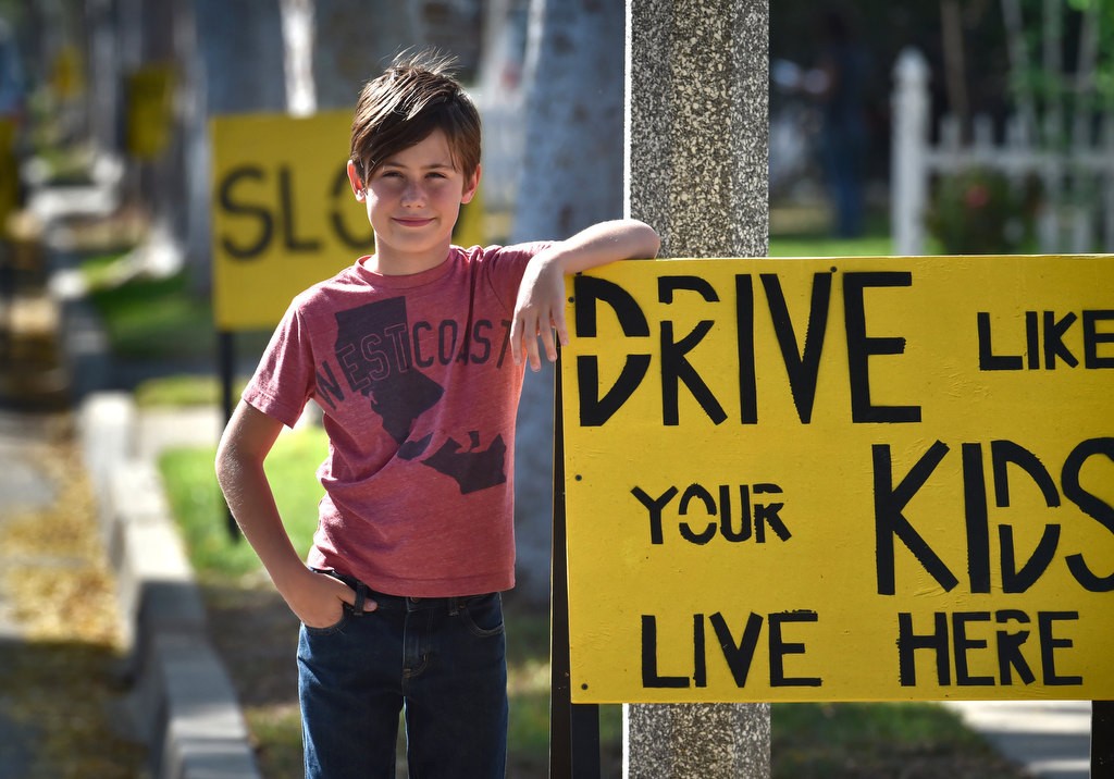 Eleven-year-old Jude Varieur of Fullerton with the signs he created to tell drivers on his street to slow down. Photo by Steven Georges/Behind the Badge OC