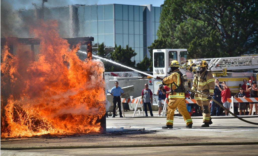 Orange City Firefighter Cole Ingle, left, and Anaheim Fire & Rescue Engineer Neil Powers extinguish a wooden shed set on fire as a demonstration for visitors, far right, attending the Fire Service Day 2016 at the North Net Fire Training Center in Anaheim.  Photo by Steven Georges/Behind the Badge OC