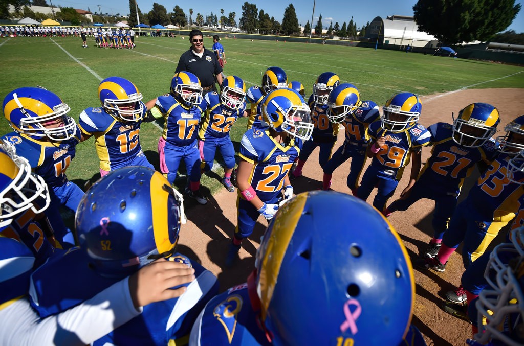 Brandon Sepulveda (27), center, gets the Anaheim Rams pumped up at the start of their Pop Warner football game with Anaheim PD Officer, and Coach, Eddie Fletcher behind them. Photo by Steven Georges/Behind the Badge OC
