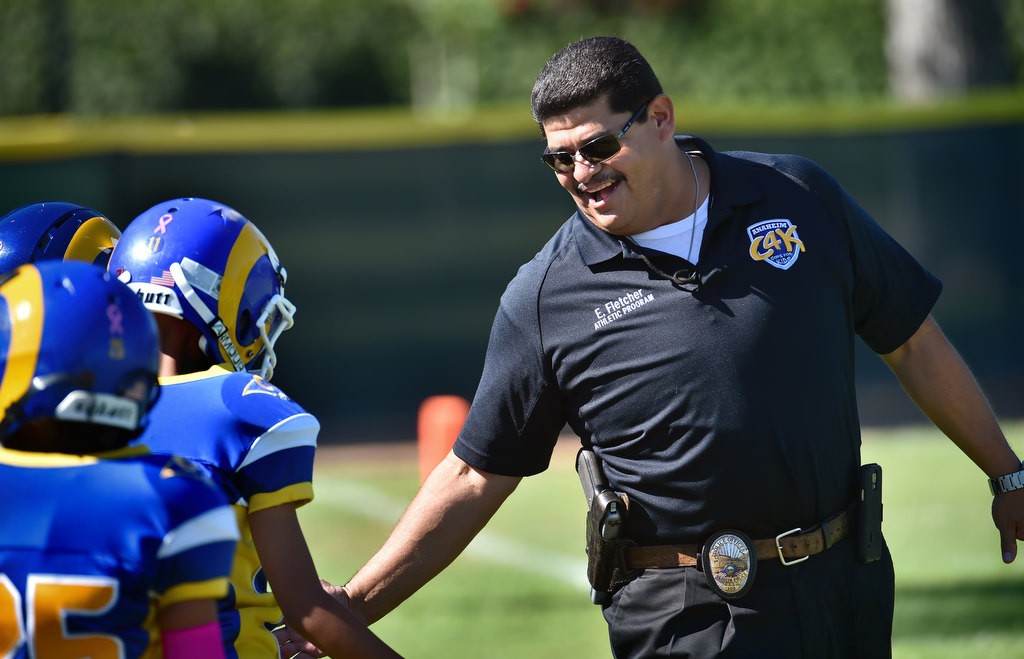Anaheim PD Officer Eddie Fletcher, one of the coaches for the Anaheim Rams, gives his players high-fives after the Pop Warner football team scored. Photo by Steven Georges/Behind the Badge OC