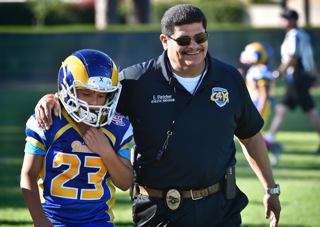 Anaheim PD Officer Eddie Fletcher, one of the coaches for the Anaheim Rams, walks with John Michael Quiroz (23) at the conclusion of a Pop Warner football game at Brookhurst Community Park in Anaheim. Photo by Steven Georges/Behind the Badge OC