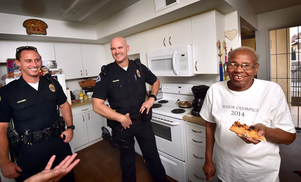 Anaheim resident Mae Hawthorne smiles while holding on to her pizza after Anaheim PD officers Brendan Thomas, left, and Brian Downs brought made a followup visit to her home to see if she was alright. Photo by Steven Georges/Behind the Badge OC